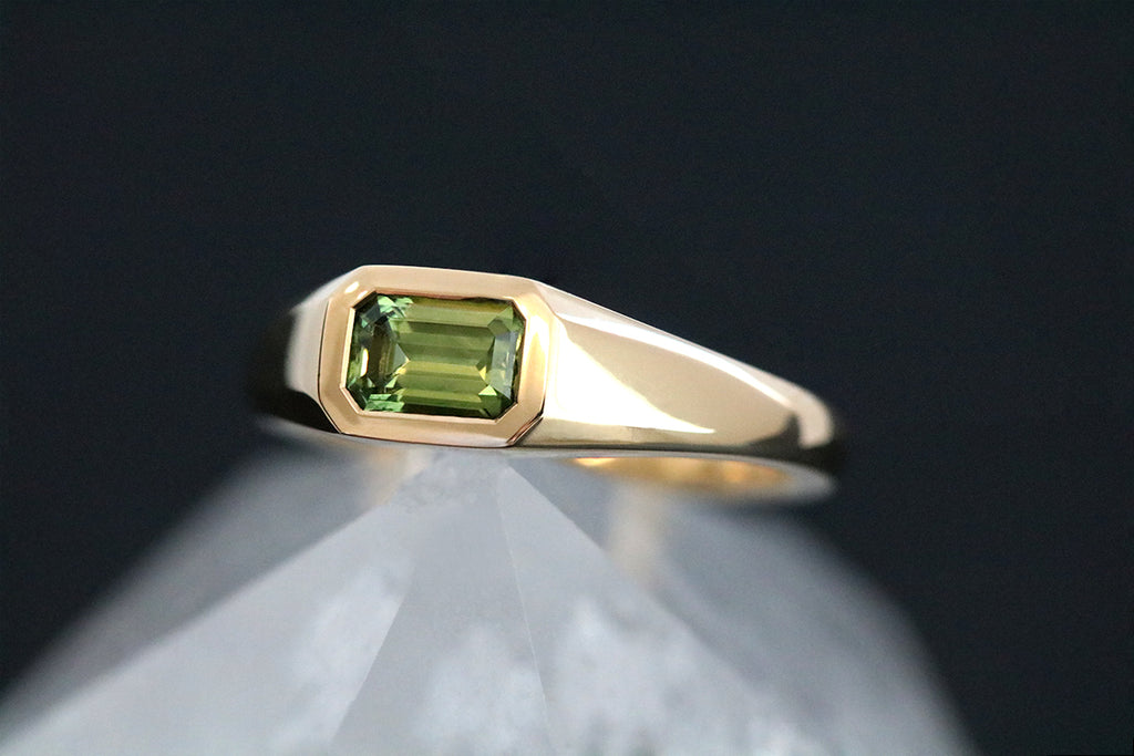 This yellow gold signet ring features a bezel set Emerald Cut Australian Sapphire, in east-west orientation. Perfectly showcasing the unique beauty of Australian sapphires, this one of a kind ring could be worn as an alternative engagement ring, or simply as a cherished everyday ring.
