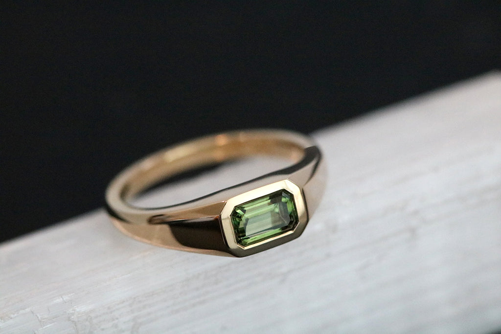 This yellow gold signet ring features a bezel set Emerald Cut Australian Sapphire, in east-west orientation. Perfectly showcasing the unique beauty of Australian sapphires, this one of a kind ring could be worn as an alternative engagement ring, or simply as a cherished everyday ring.