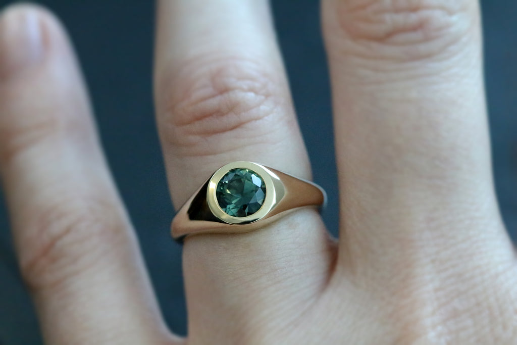 This yellow gold signet ring features a bezel set Round Brilliant Cut Australian Sapphire. Perfectly showcasing the unique beauty of Australian sapphires, this one of a kind ring could be worn as an alternative engagement ring, or simply as a cherished everyday ring.